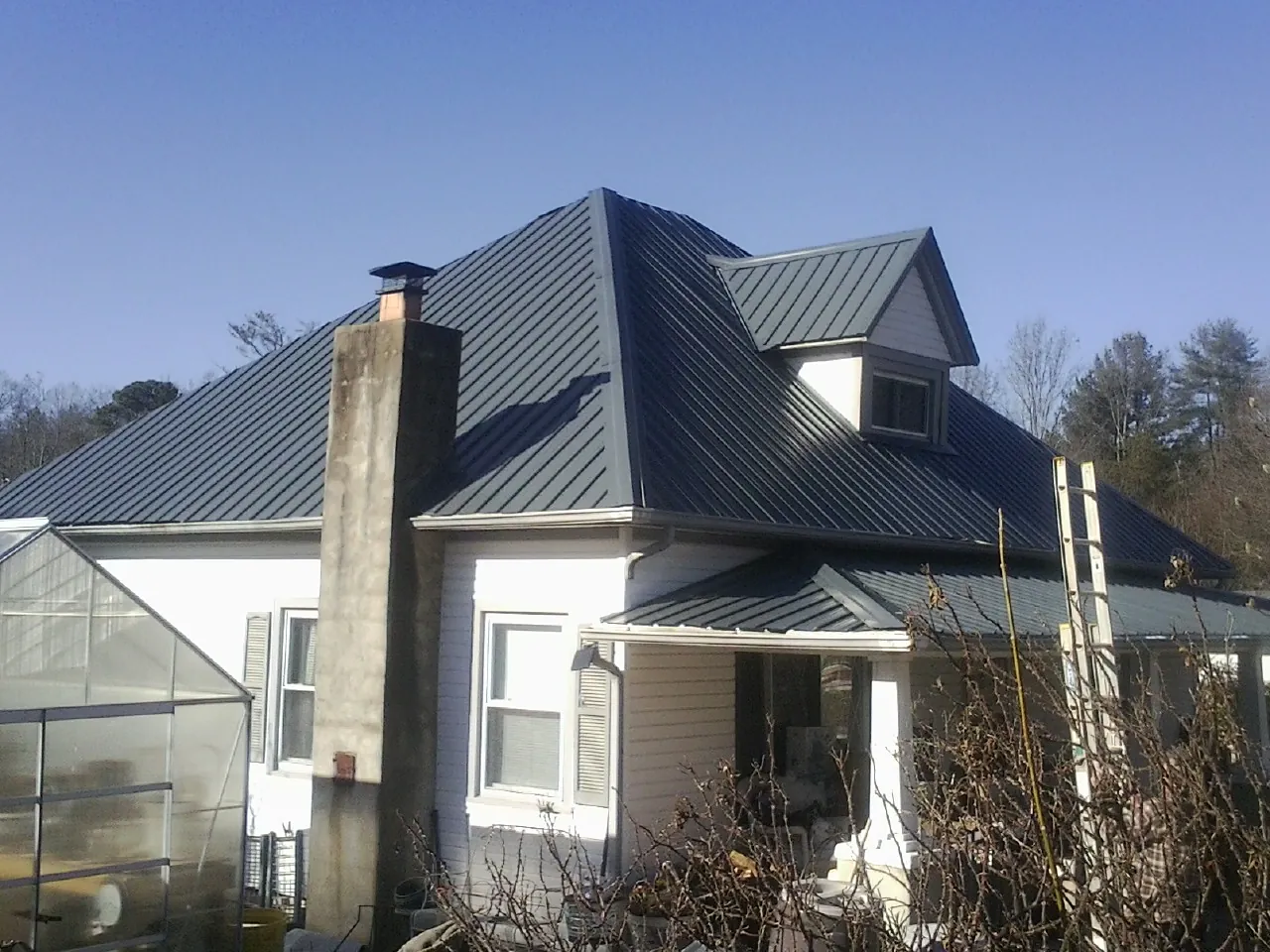 Dark blue standing seam metal roof on a white farmhouse with dormer — Slate & Tile Roof Repair by Roofing Brothers in Hubert