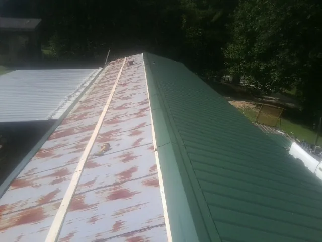Old rusted panels beside newly installed green metal roofing — Wind Damage Roof Repair by Roofing Brothers in Hubert