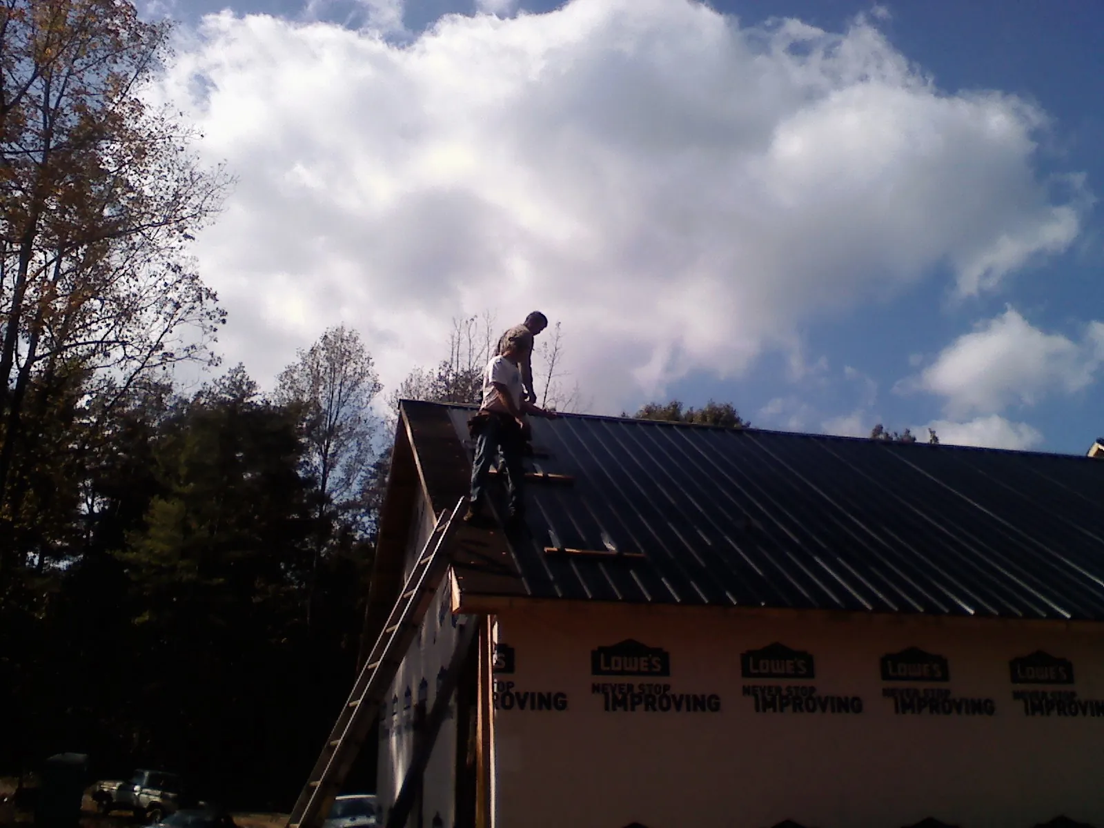 Roofer fastening dark metal panels high against a cloudy sky, from a Roof Inspection job in Hubert