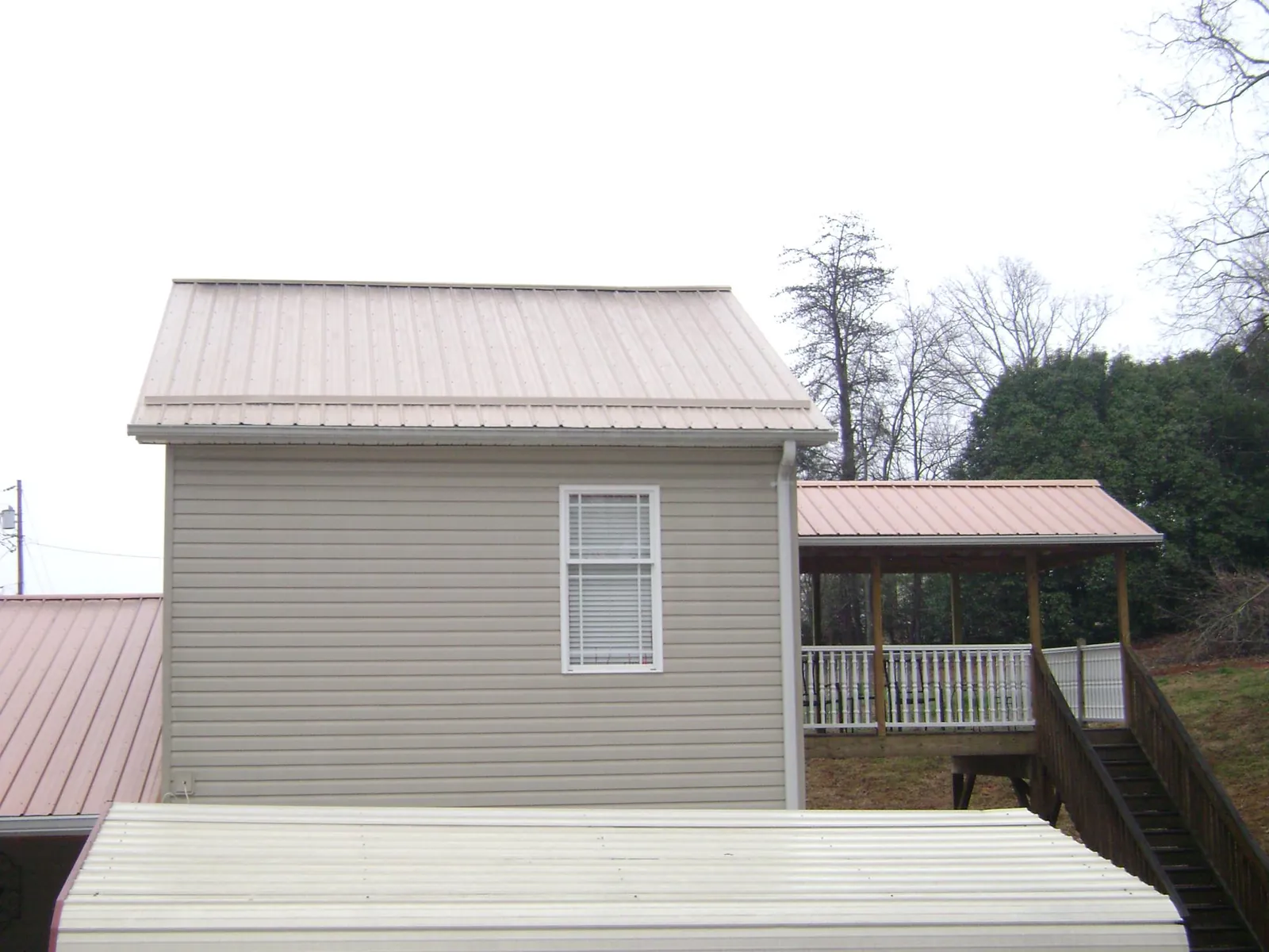 Tan metal roofs on a two story addition and attached porch, from a Roof Replacement job in Hubert